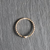 A thin gold beaded ring with a small central connector, displayed on a textured gray slate surface.