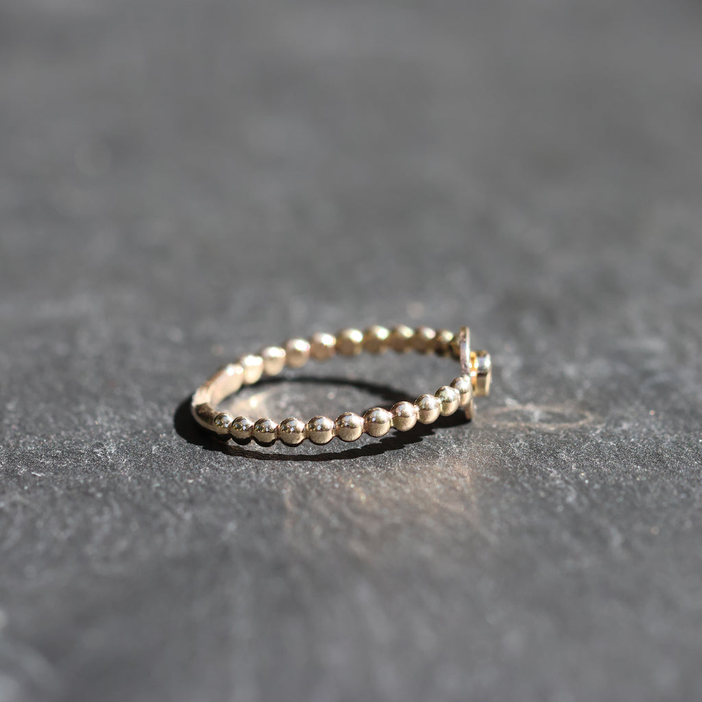 A delicate gold beaded ring with a small star-shaped accent on the side, resting on a textured dark gray slate surface.