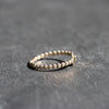 A delicate gold beaded ring with a small star-shaped accent on the side, resting on a textured dark gray slate surface.